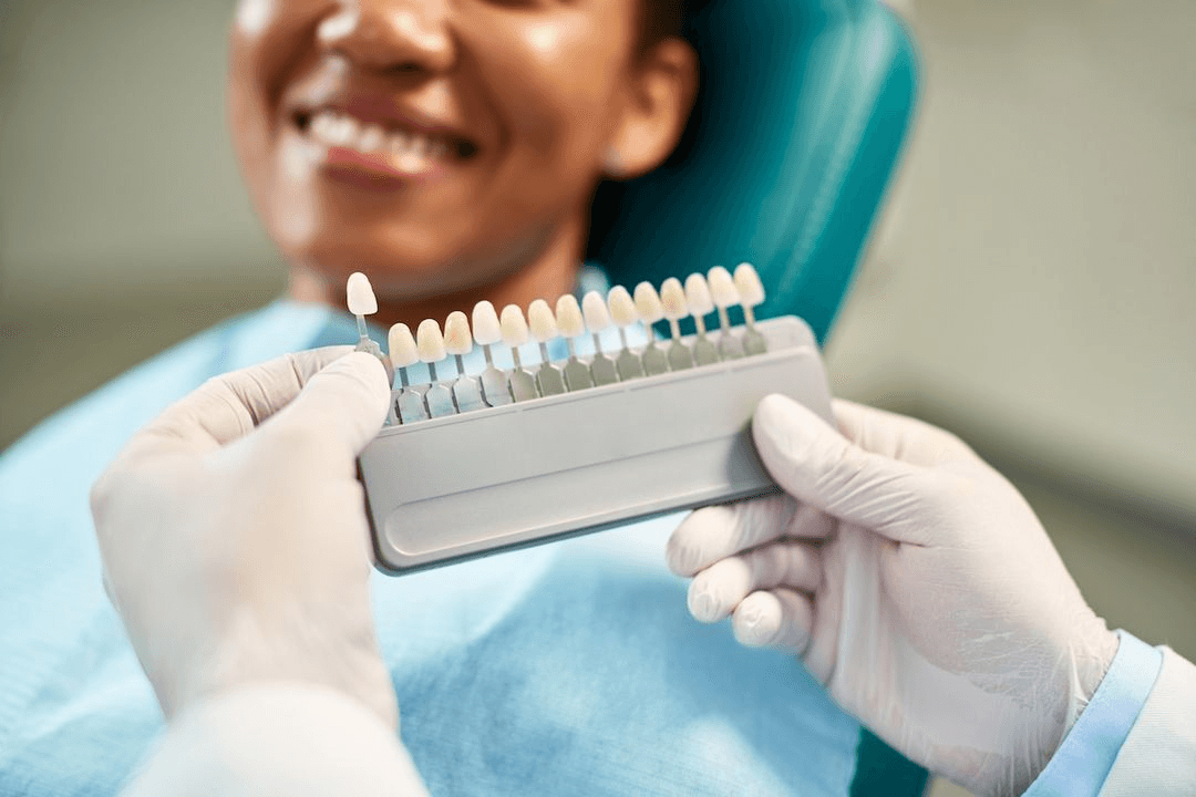 Dentist holding porcelain veneer shade guide for smiling patient at Esthetique Dentistry Ashburn