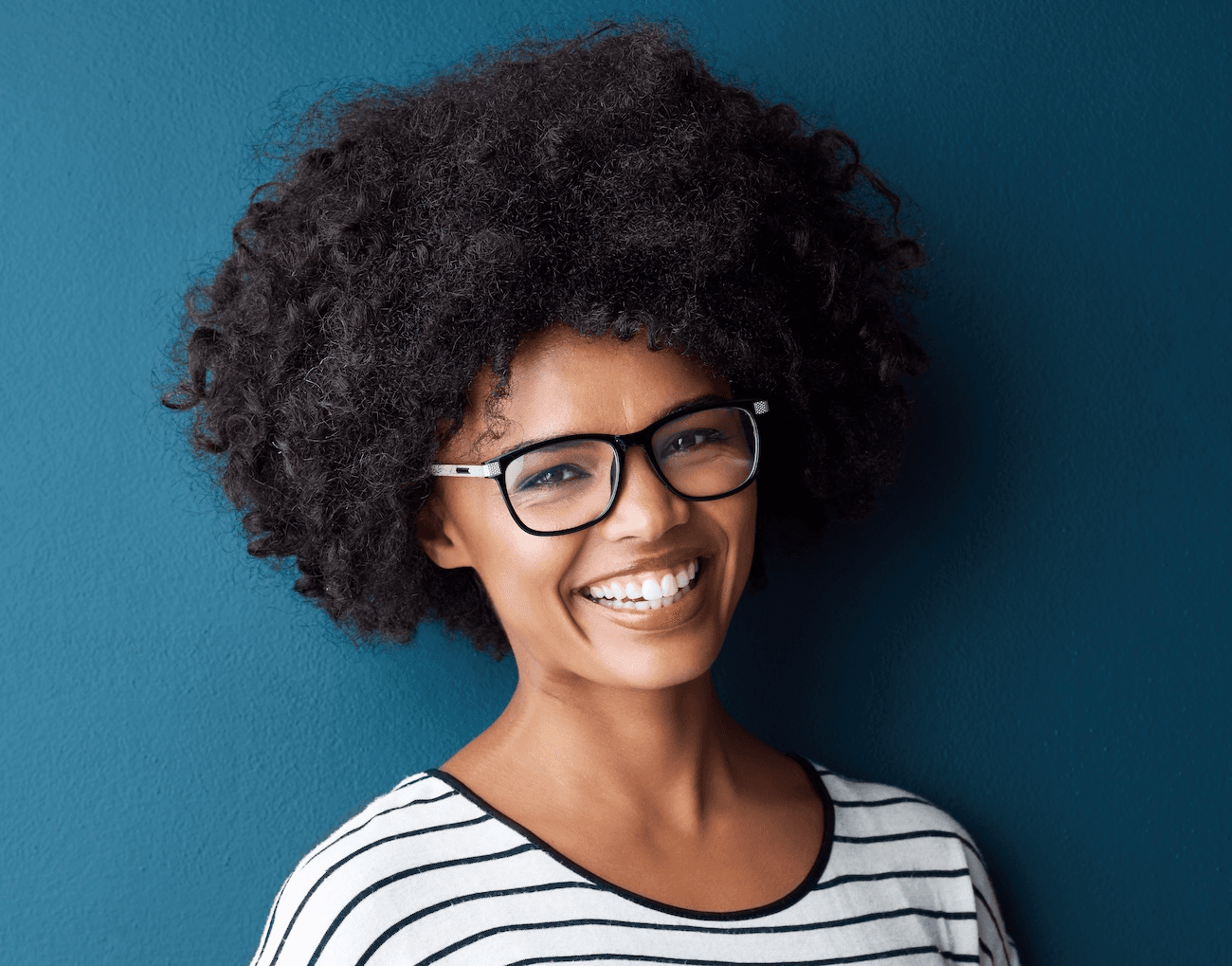 Young woman with natural hair and glasses smiling brightly after Zoom whitening at Esthetique Dentistry Ashburn